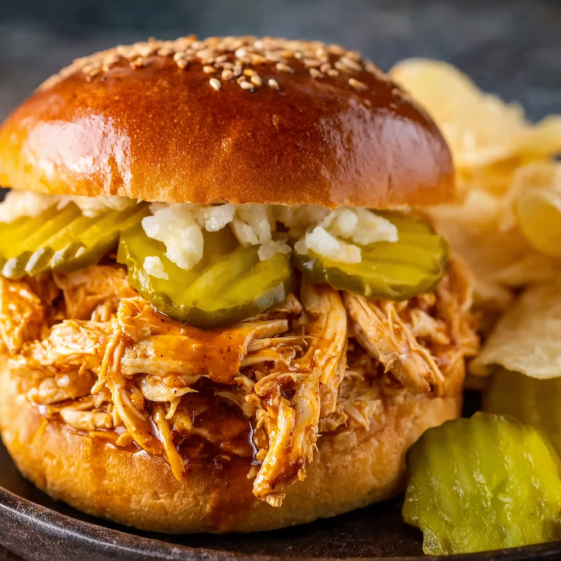 A close up of a sandwich with pickles and barbecue sauce.
