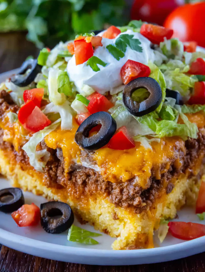 A delicious cornbread taco bake with lettuce, tomatoes, and olives.