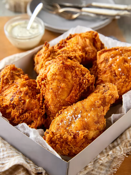A box of fried chicken with a dipping sauce.