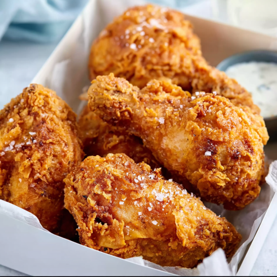 A box of fried chicken with a dipping sauce.