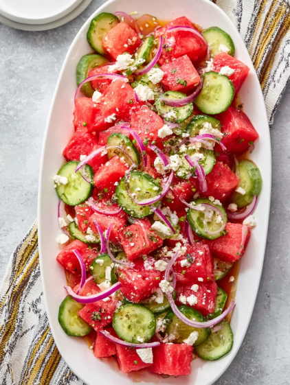 A white bowl filled with watermelon, cucumbers, and onions.