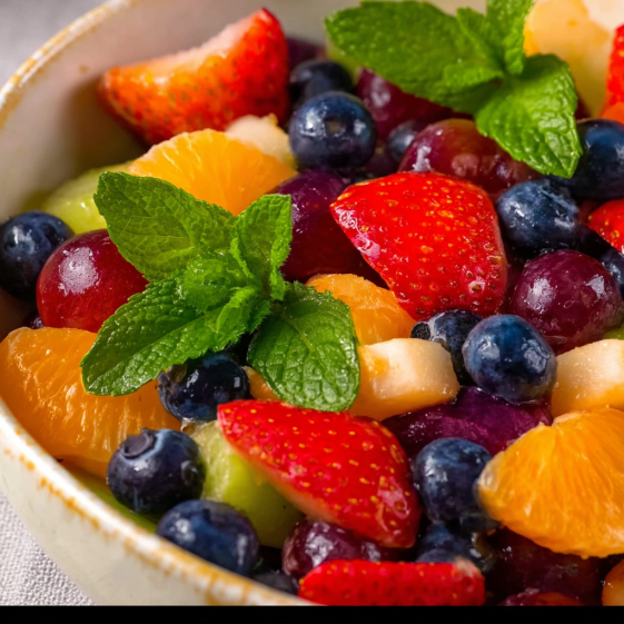 A bowl of fruit salad with strawberries, blueberries, oranges, and mints.
