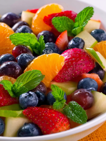 A bowl of fruit salad with blueberries, strawberries, oranges, and mints.