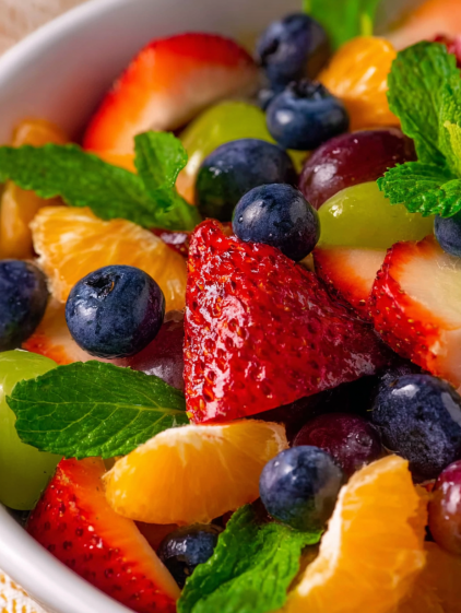 A bowl of fruit salad with strawberries, blueberries, oranges, and mints.