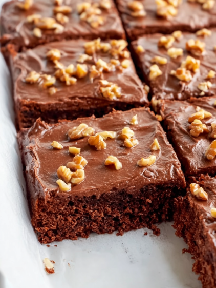 A slice of chocolate cake with nuts on top.