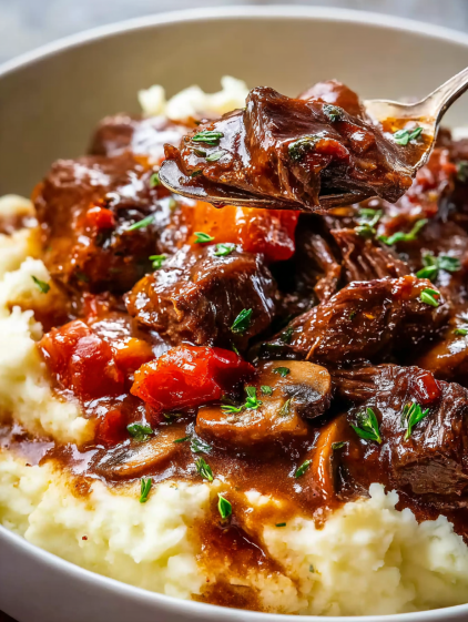 A bowl of beef bourguignon with mushrooms and tomatoes.