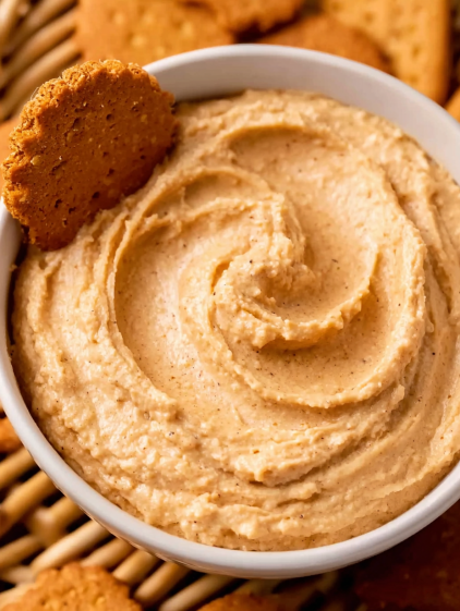 A bowl of pumpkin dip with a cookie on top.