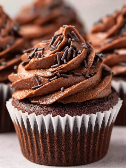 A chocolate cupcake with chocolate frosting and chocolate sprinkles.