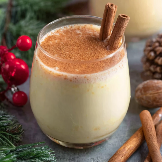 A glass of eggnog with cinnamon sticks in it.