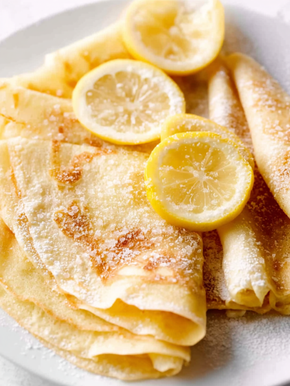 A plate of crepes with lemon wedges on top.