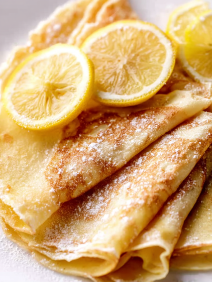 A plate of crepes with lemon wedges on top.