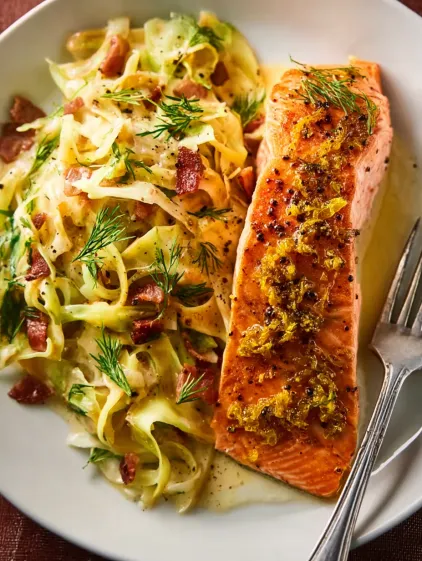 A plate of food with salmon, cabbage, and bacon.