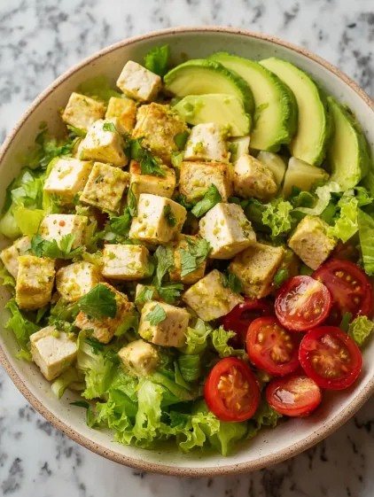 A bowl of food with tofu, lettuce, tomatoes, and avocado.