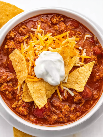 A bowl of chili with cheese and chips on top.