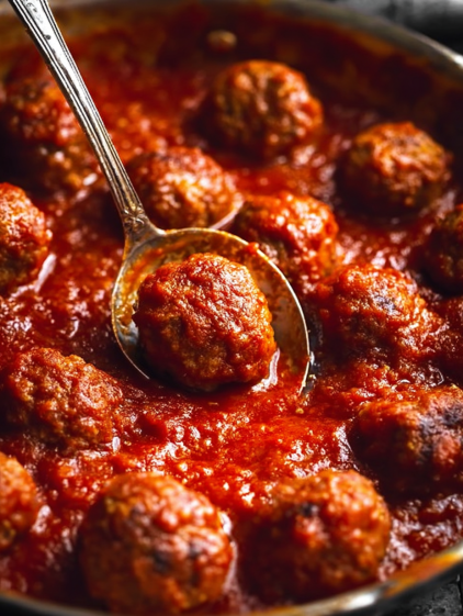 A spoon is in a bowl of meatballs.