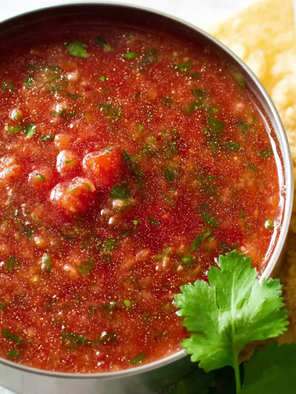 A bowl of red sauce with green herbs.
