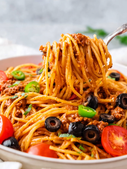 A spoon is scooping up spaghetti with meat sauce and vegetables.
