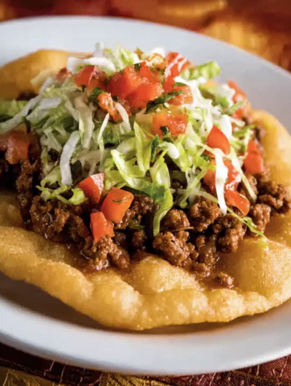 A plate of Navajo tacos with lettuce and tomatoes.