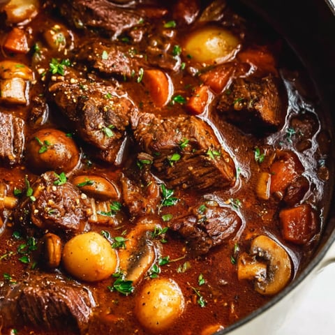 A pot of beef bourguignon with mushrooms and carrots.