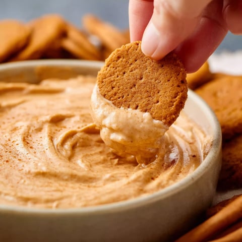 A person is dipping a cracker into a pumpkin pie dip.