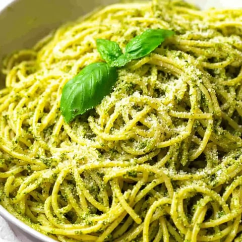 A bowl of pasta with pesto sauce.