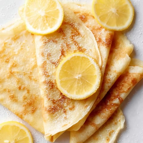 A plate of crepes with lemon wedges on top.