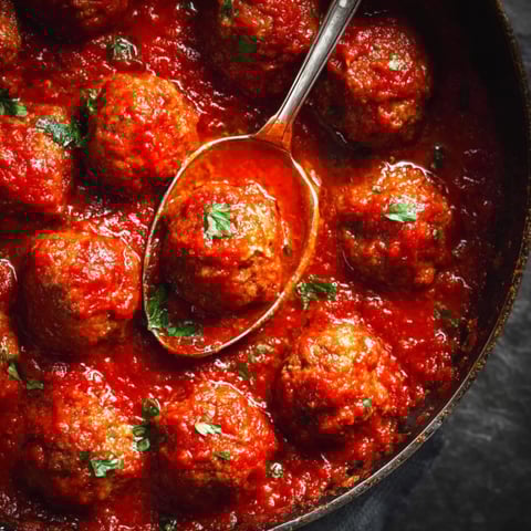 A spoon is in a bowl of meatballs.