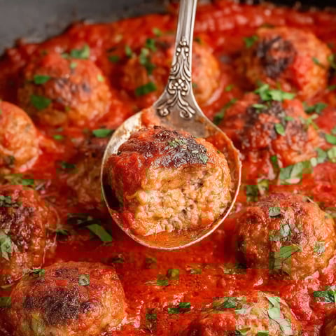A spoon is in a bowl of meatballs.