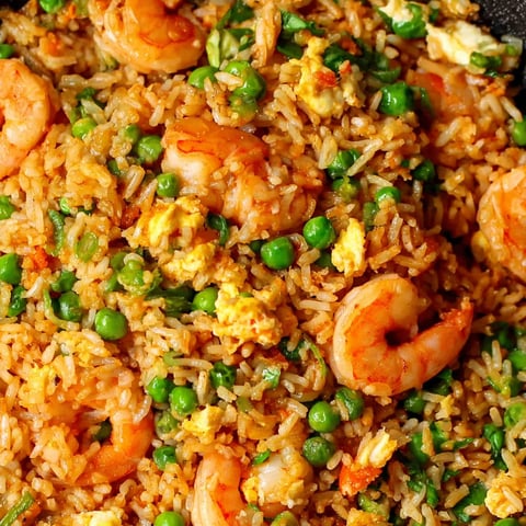 A plate of shrimp fried rice with peas and egg.