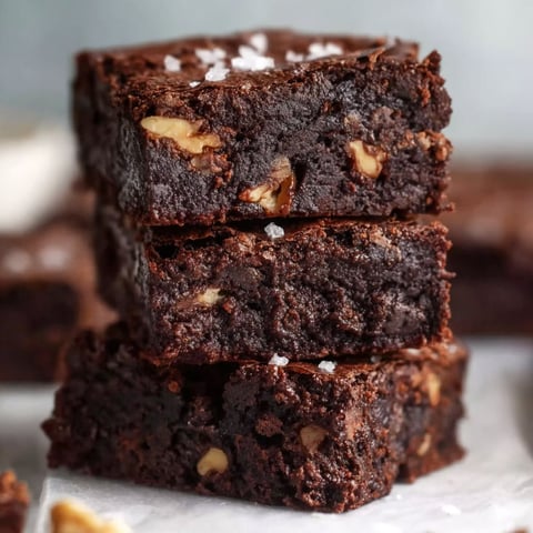 A stack of brownies with nuts on top.