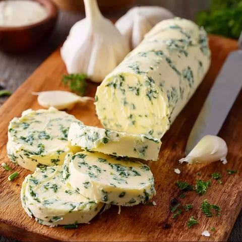 A wooden cutting board with a piece of garlic herb butter.
