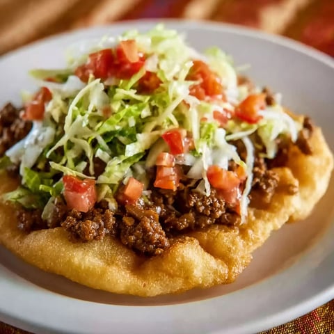 A plate of Navajo tacos with lettuce and tomatoes.